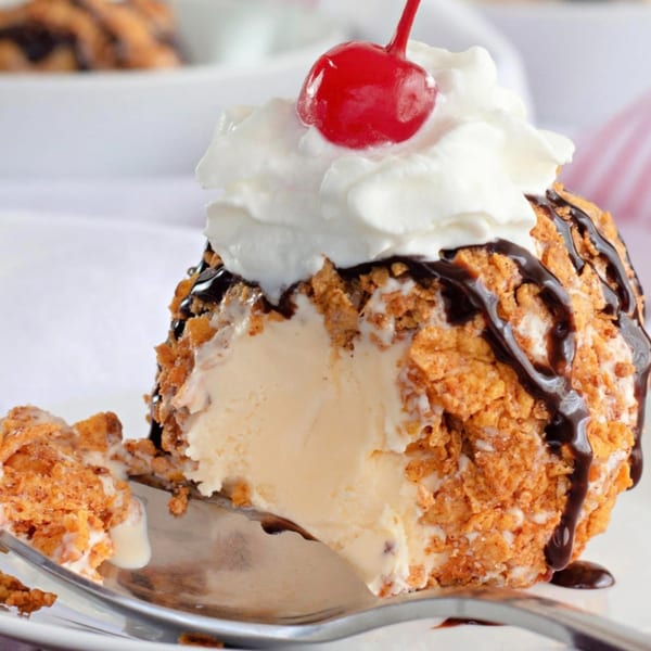 Fried ice cream dessert with a crispy coating, chocolate drizzle, whipped cream, and a cherry on top.