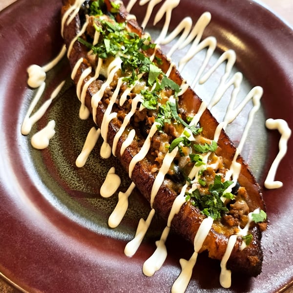 A Mexican dish of a fried plantain stuffed with ground meat, cheese, cilantro, and a creamy drizzle.