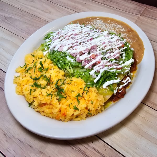A Mexican combination plate with enchiladas, rice, and refried beans, topped with lettuce, sour cream, and cheese.
