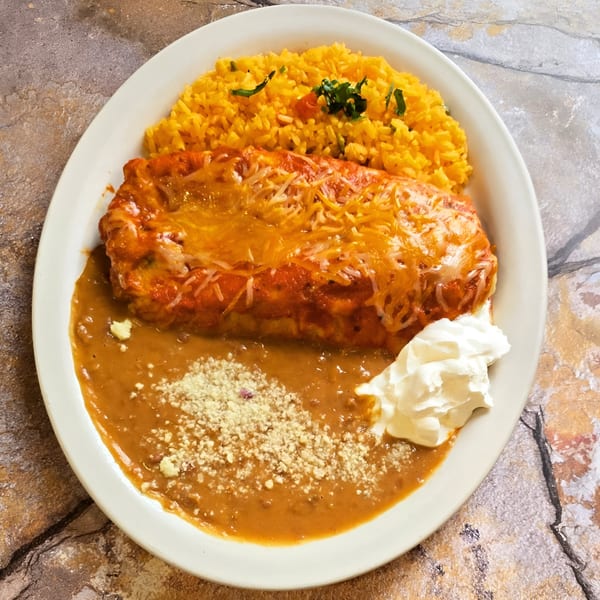 A Franco's Taqueria burrito covered in red sauce and melted cheese, with yellow rice, refried beans, and sour cream.