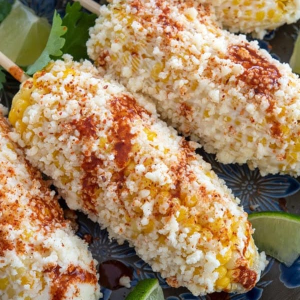 Three Franco's Taqueria elotes, Mexican street corn, on a blue plate with lime wedges.
