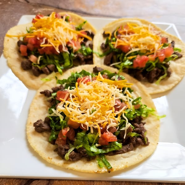 Three Franco's Taqueria tacos with beef, lettuce, diced tomatoes, and shredded cheese on a white plate.