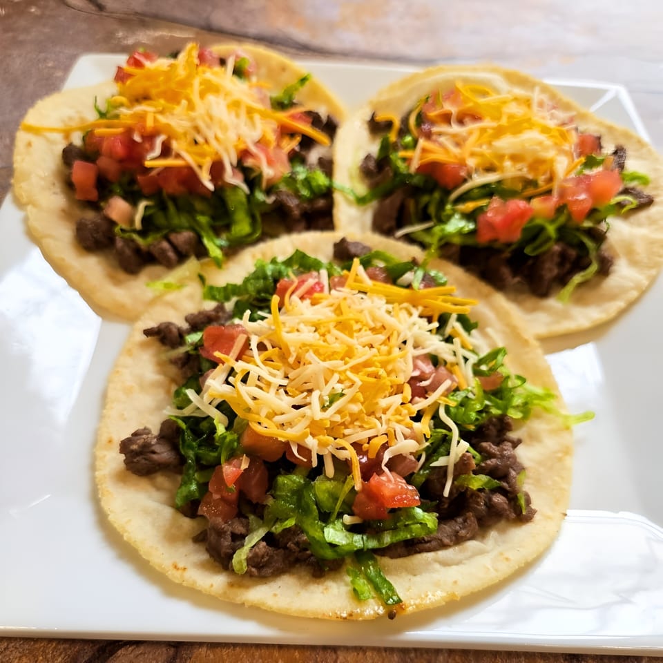 Three Franco's Taqueria tacos with beef, lettuce, diced tomatoes, and shredded cheese on a white plate.