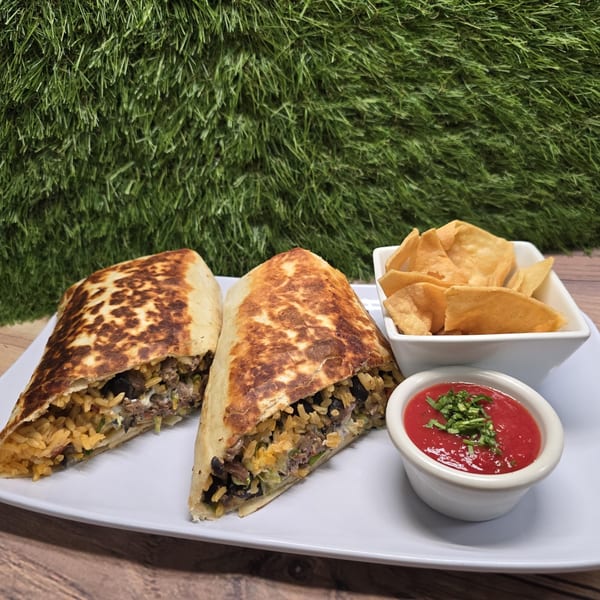 Two Franco's Taqueria burritos, chips, and salsa on a white plate against a green and wood background.