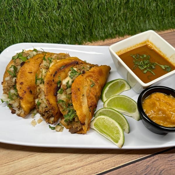 Four Franco's Taqueria birria tacos with lime wedges, consommé, and salsa on a white plate.